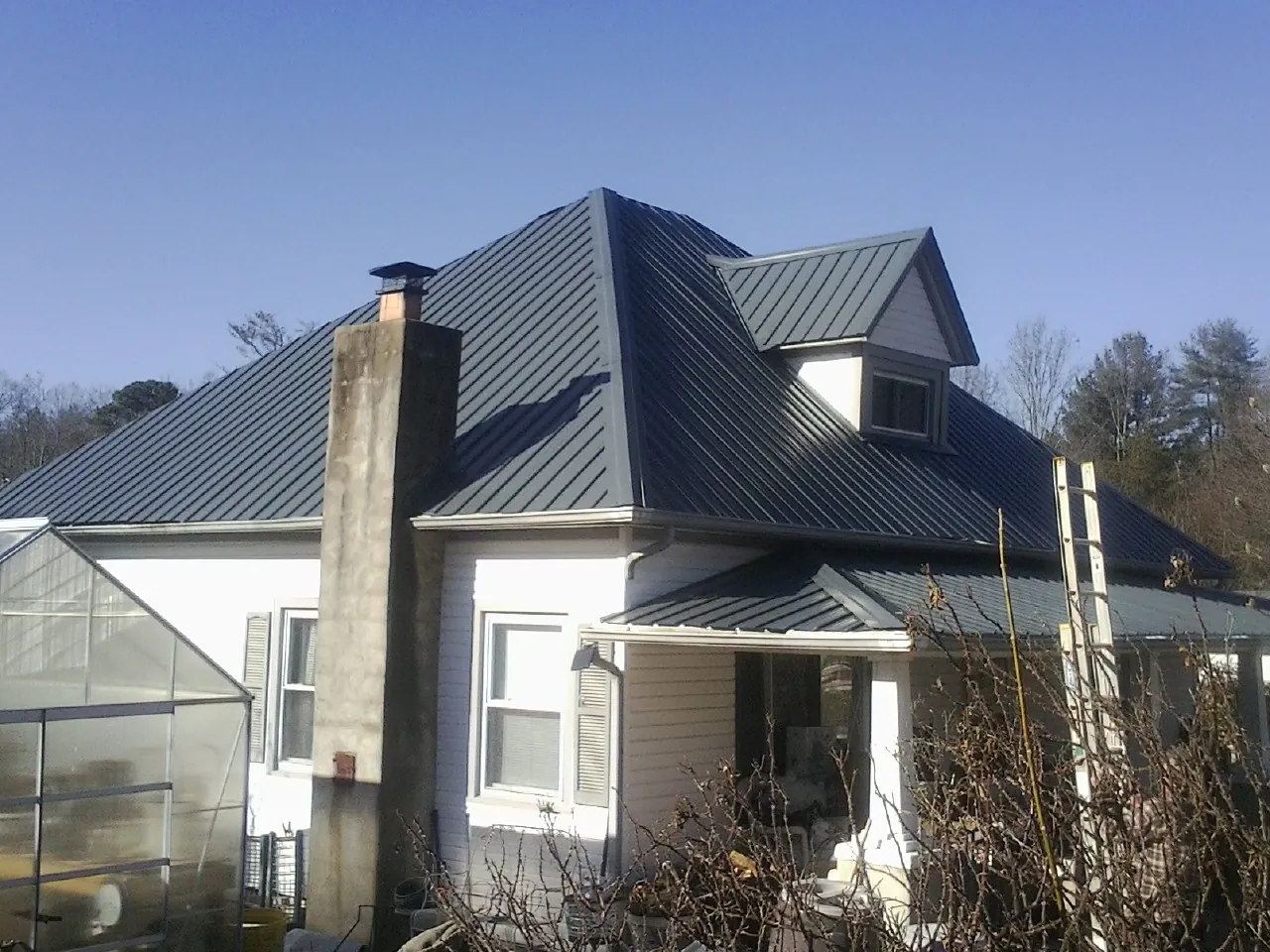 Dark blue standing seam metal roof on a white farmhouse with dormer — Slate & Tile Roof Repair by Roofing Brothers in Pitcher