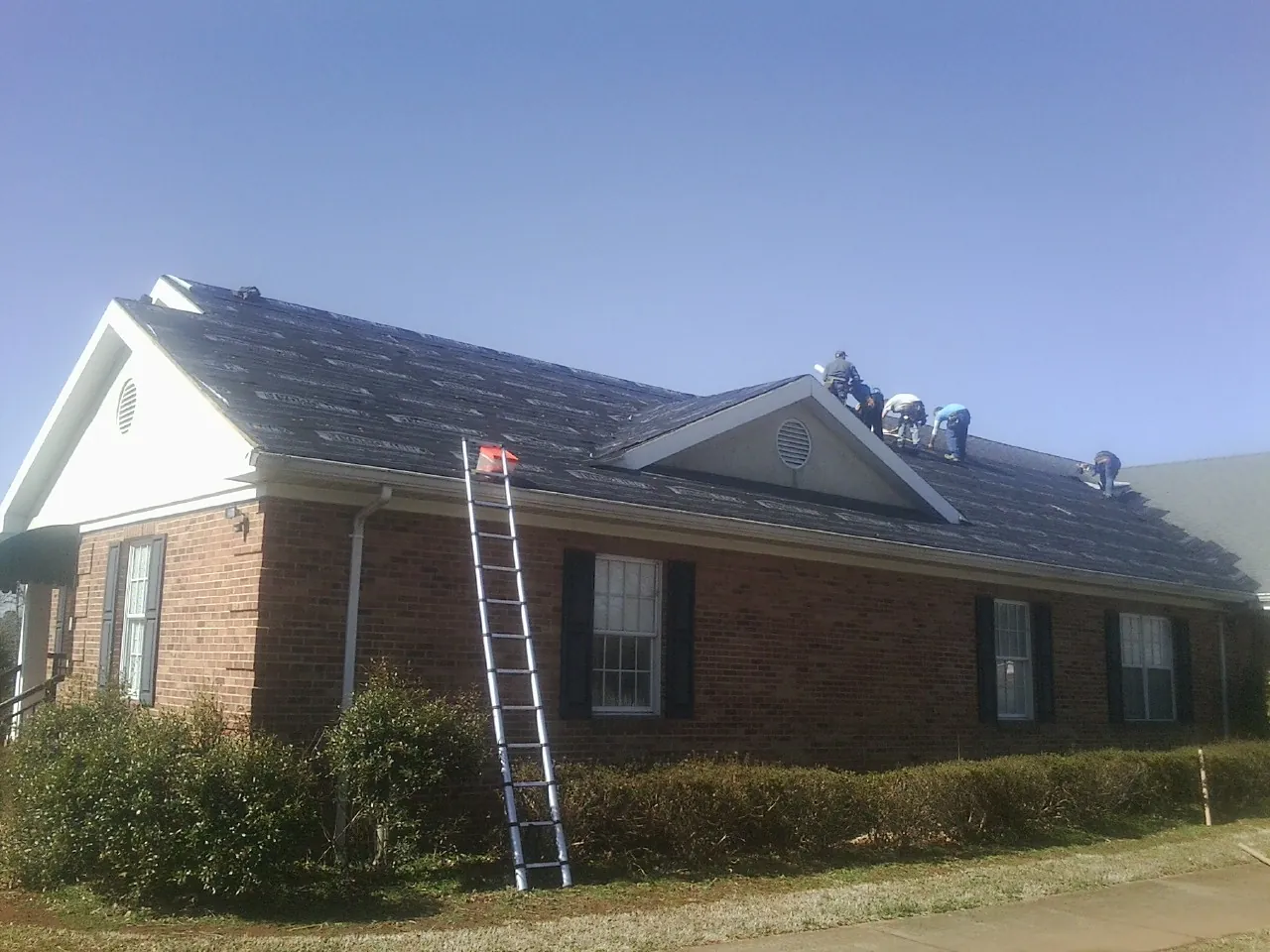 Crew tearing shingles off a brick ranch roof with a ladder set — Metal Roof Repair work by our crew in Pitcher