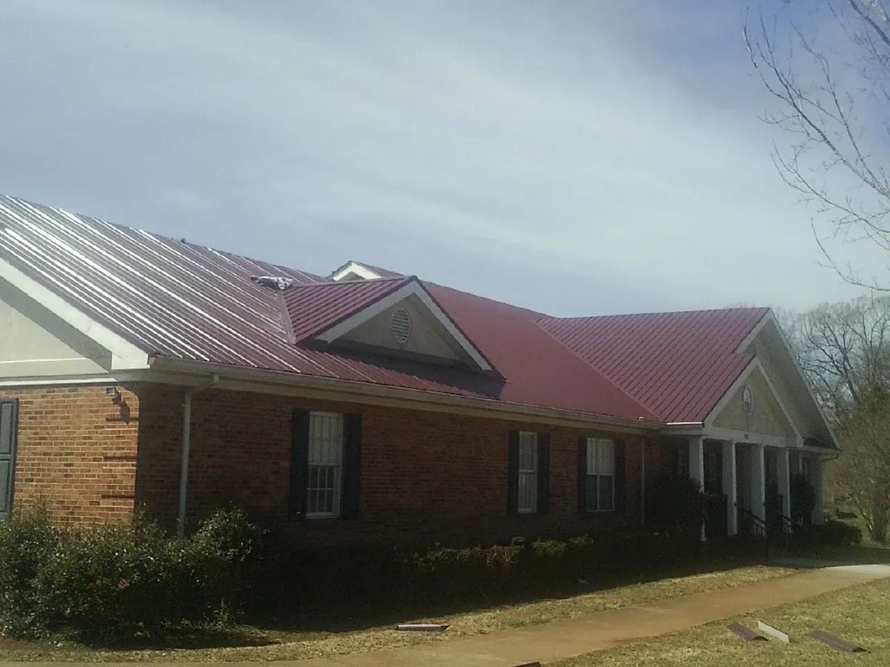 Red metal roof with gabled entries on a long brick building, from a Hail Damage Roof Repair job in Pitcher