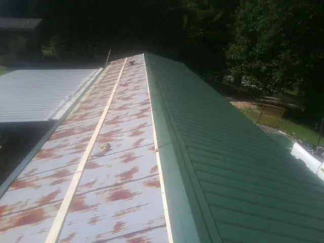 Old rusted panels beside newly installed green metal roofing — Wind Damage Roof Repair by Roofing Brothers in Pitcher