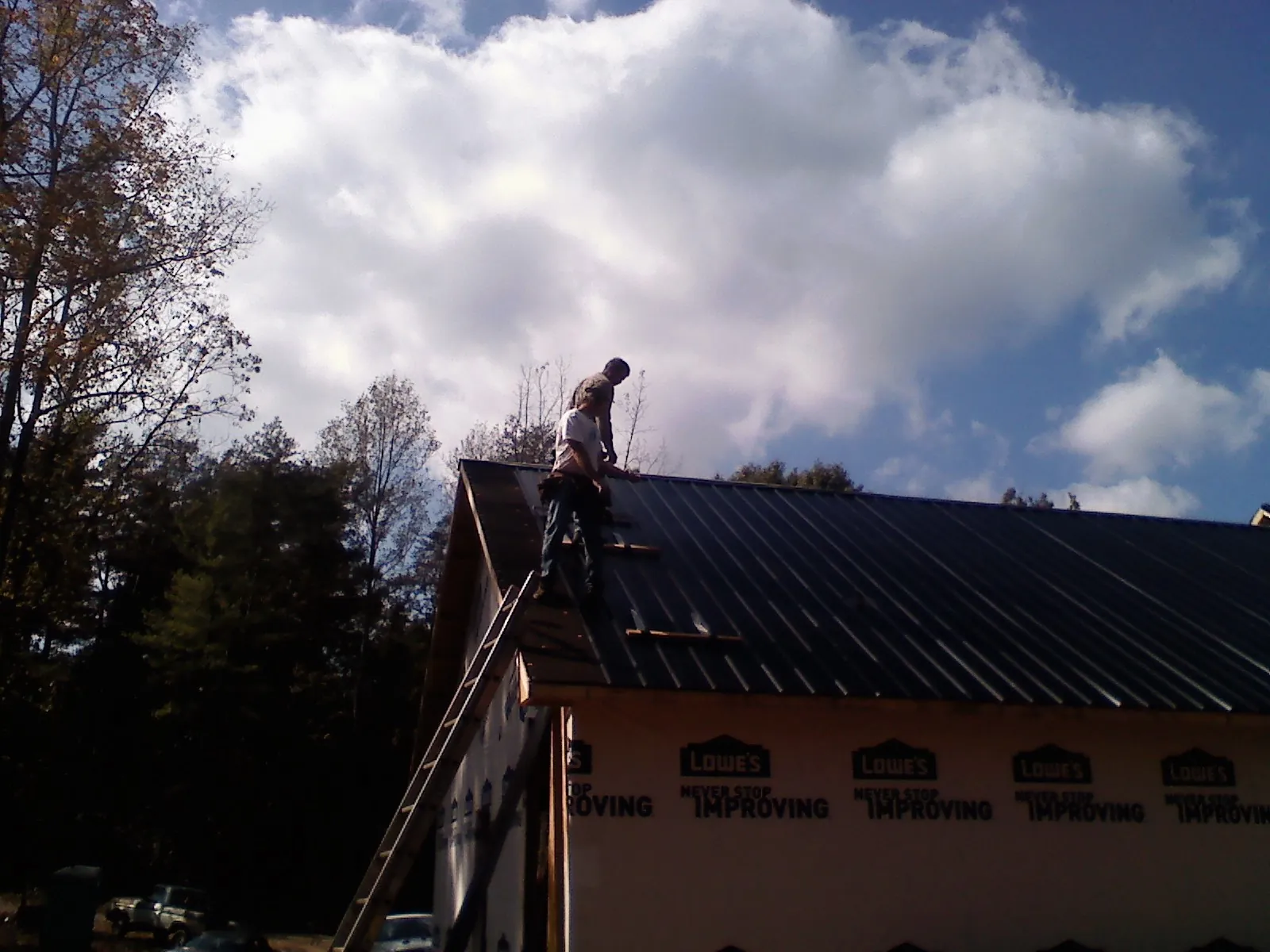 Roofer fastening dark metal panels high against a cloudy sky, from a Roof Inspection job in Pitcher