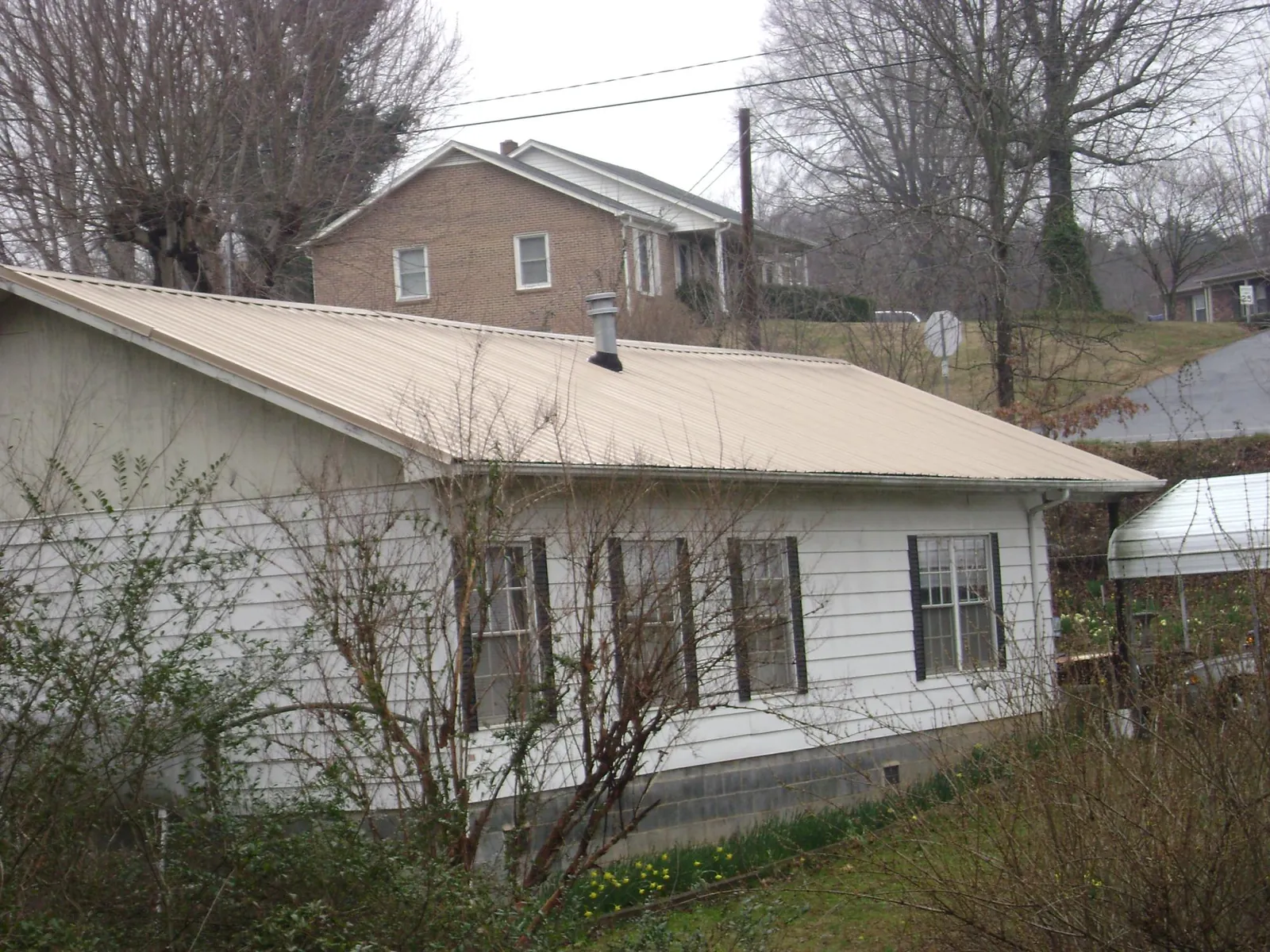 Tan metal roof on a white sided house set into a hillside — Commercial Roofing by Roofing Brothers in Pitcher